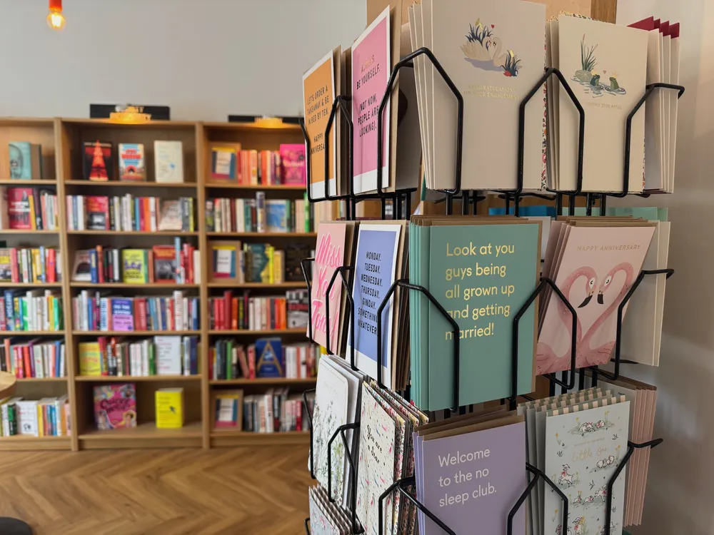 A spinner of greetings cards in the shop, the fiction shelves behind