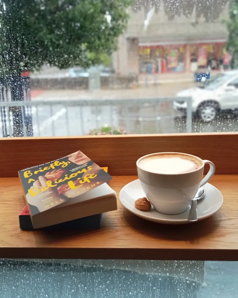 A cappuccino and a paperback on the window ledge, with rain on the glass and the High Street beyond