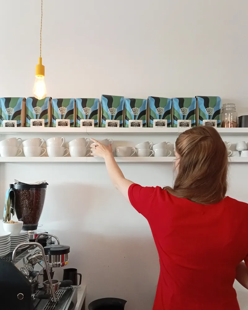 A bookseller in a red dress reaching for a cup from the shelf above the coffee machine