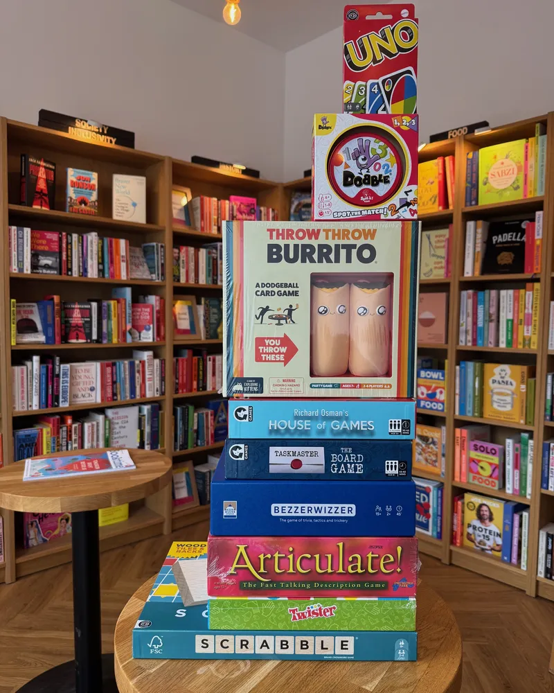 A tower of board games on a round table, Scrabble at the bottom and Uno on top, with Articulate, Taskmaster and Dobble between