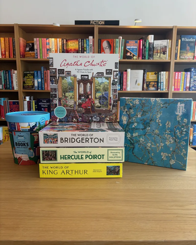 Jigsaw boxes stacked on the table: The World of Agatha Christie, Bridgerton, Hercule Poirot and King Arthur, with a Van Gogh almond blossom puzzle beside them