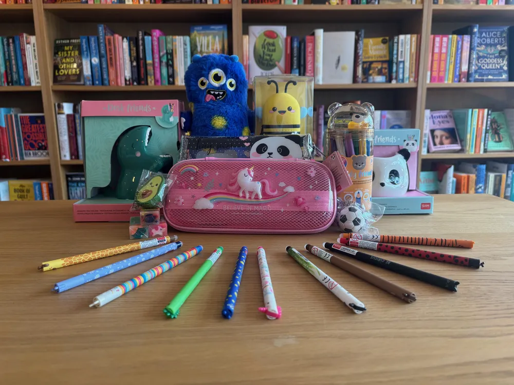 Patterned pens fanned across the table beside a unicorn pencil case, a dinosaur desk tidy and a blue monster soft pencil case
