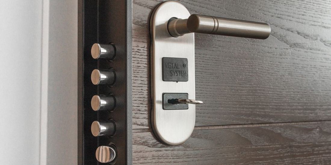 A multipoint door lock seen with the door open — the row of locking bolts down the edge of the door and the handle and cylinder on the face
