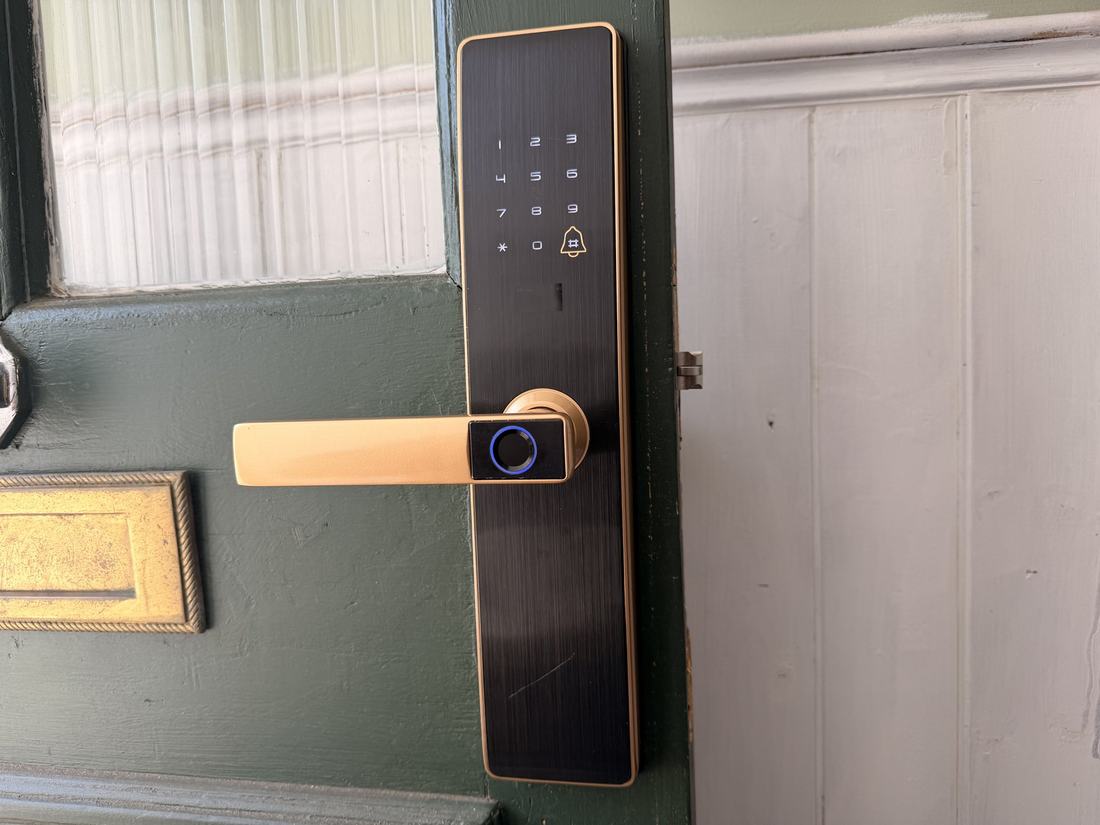 The finished smart lock fitted to the green timber door, showing the illuminated keypad and the fingerprint reader set into the handle.