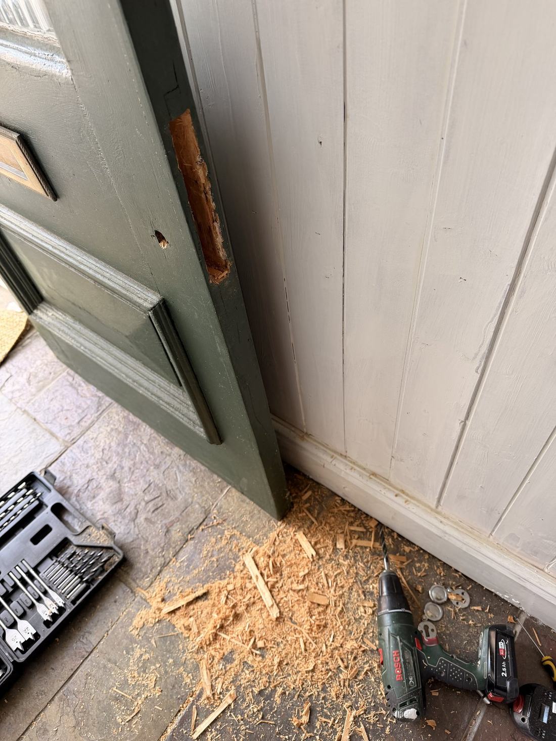 The pocket for a lock body cut into the edge of a timber front door during one of our installations, with the door open and tools on the step